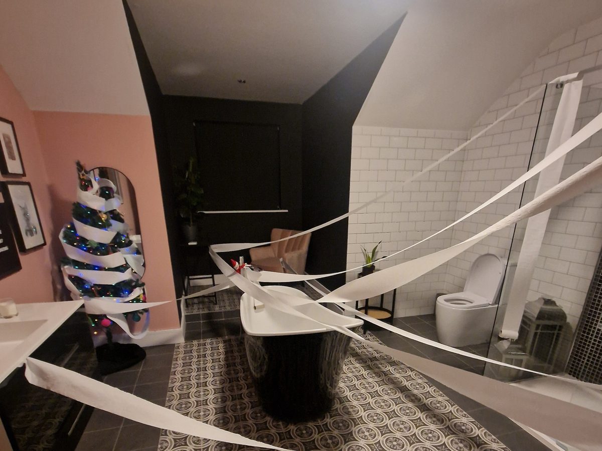 Elf in decorated bathroom with festive garland and holiday embellishments.