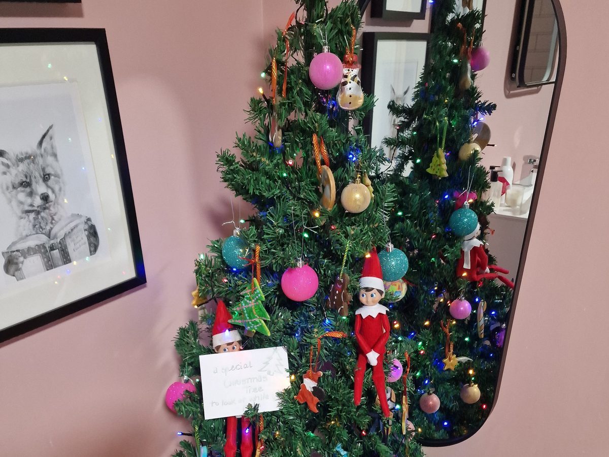Elf decorating small tree in bathroom with candy cane ornament.