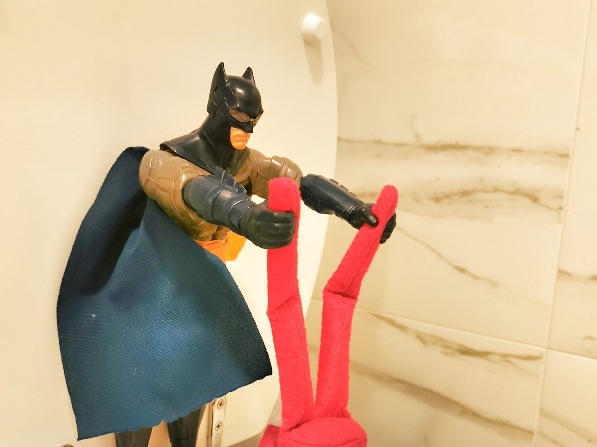 Batman action figure bathing elf in toilet with tiny washcloth and hygiene supplies.