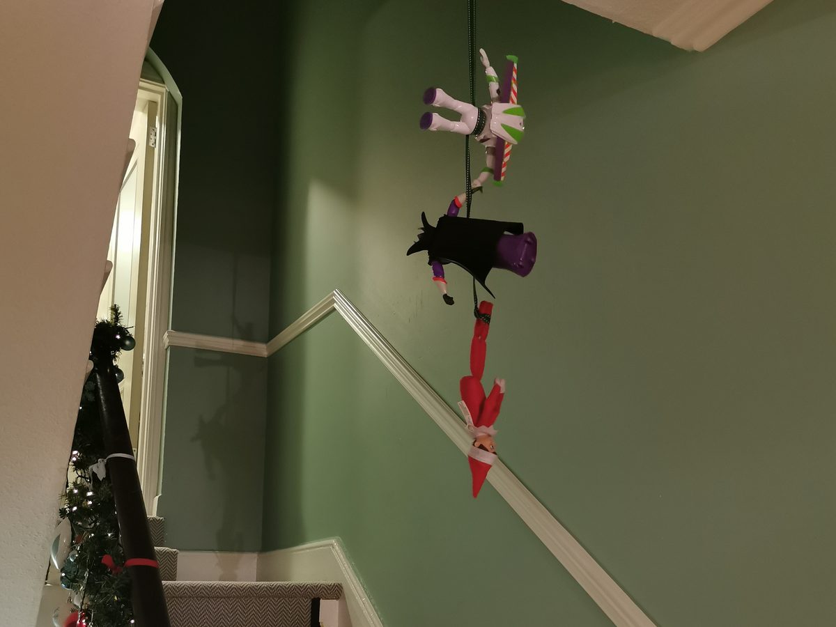 Elf wrapped in tape with Buzz Lightyear action figure positioned to rescue.