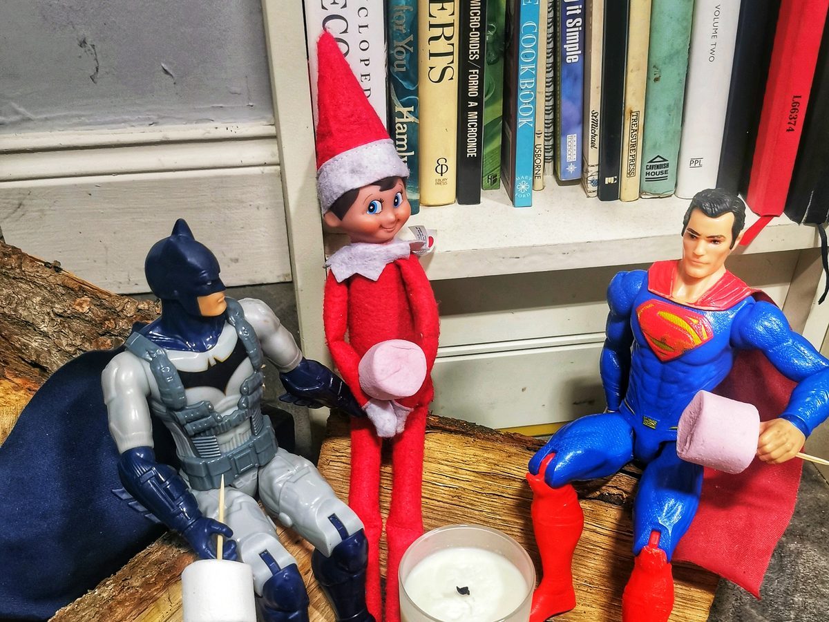 Elf roasting marshmallows with superhero action figures around pretend campfire.