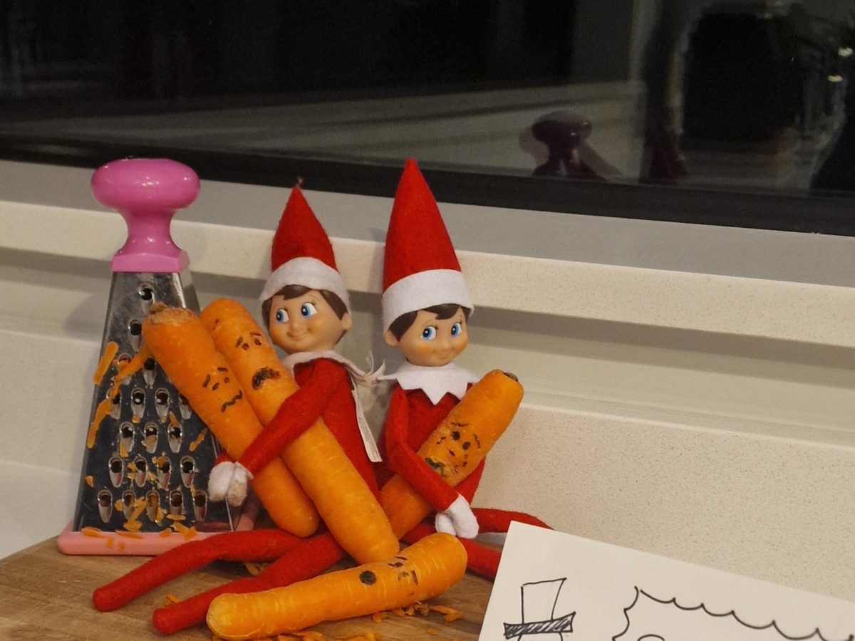Elf with collection of baby carrots arranged as melted snowman noses.