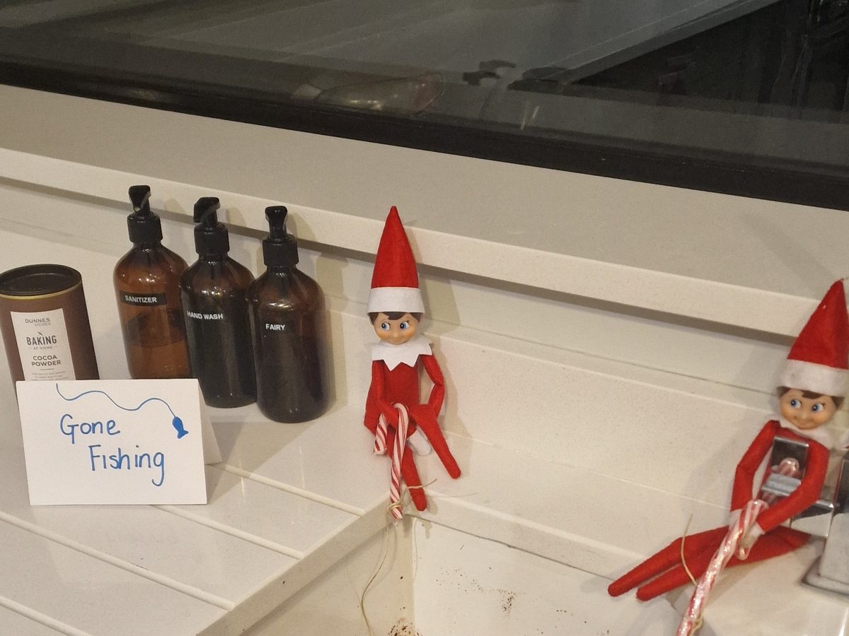 Elf fishing in sink filled with cocoa powder water with toy fishing rod.