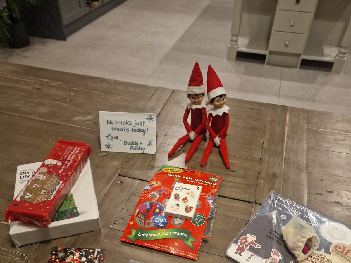 Elf positioned beside wrapped craft kits and activity supplies as gift delivery.