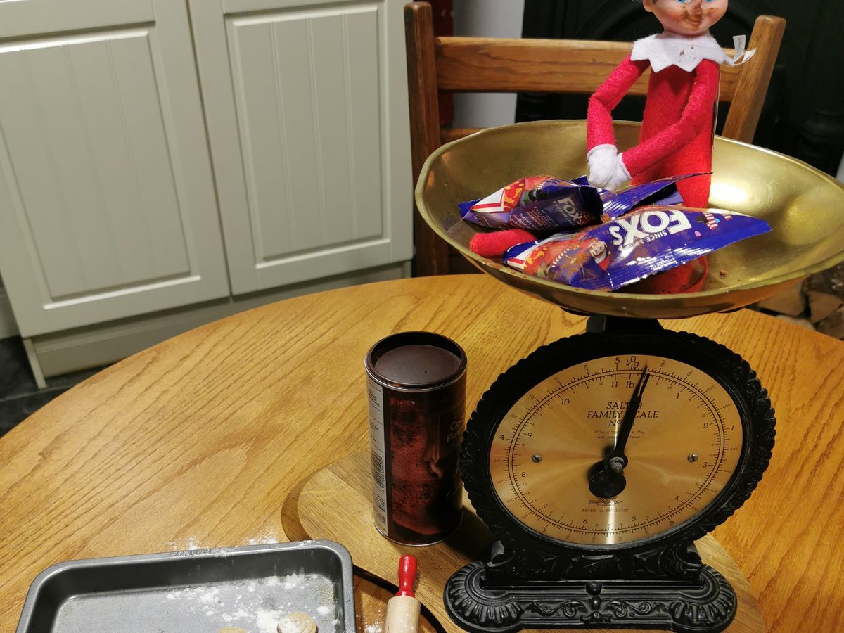 Elf covered in flour next to cookie tray on kitchen counter.