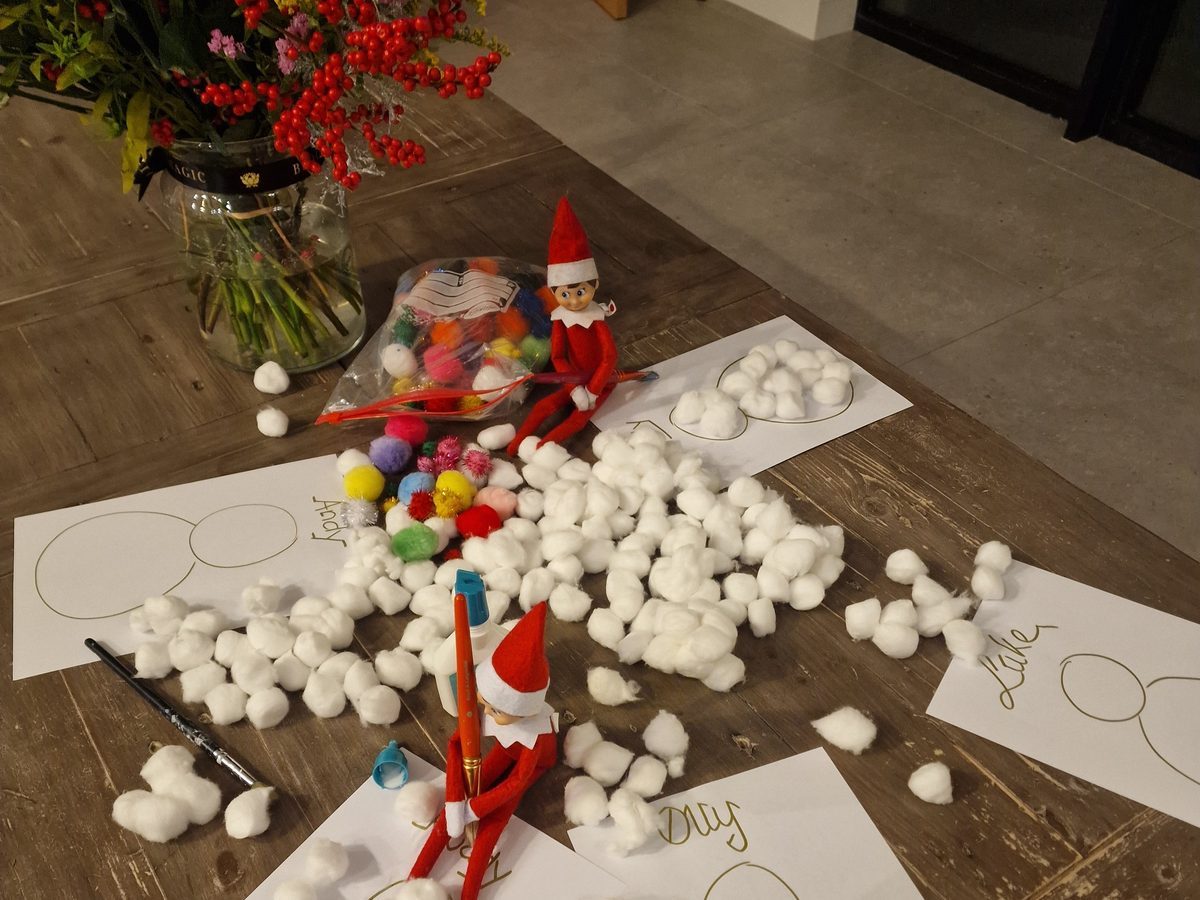 Elf surrounded by craft supplies including glitter, glue, and colorful paper.