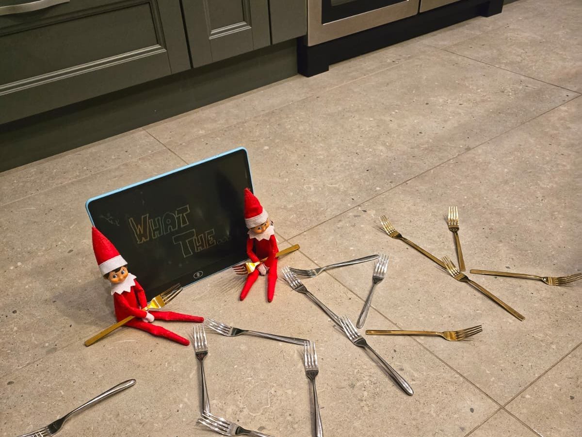 Elf standing in open cutlery drawer surrounded by standing forks and spoons.