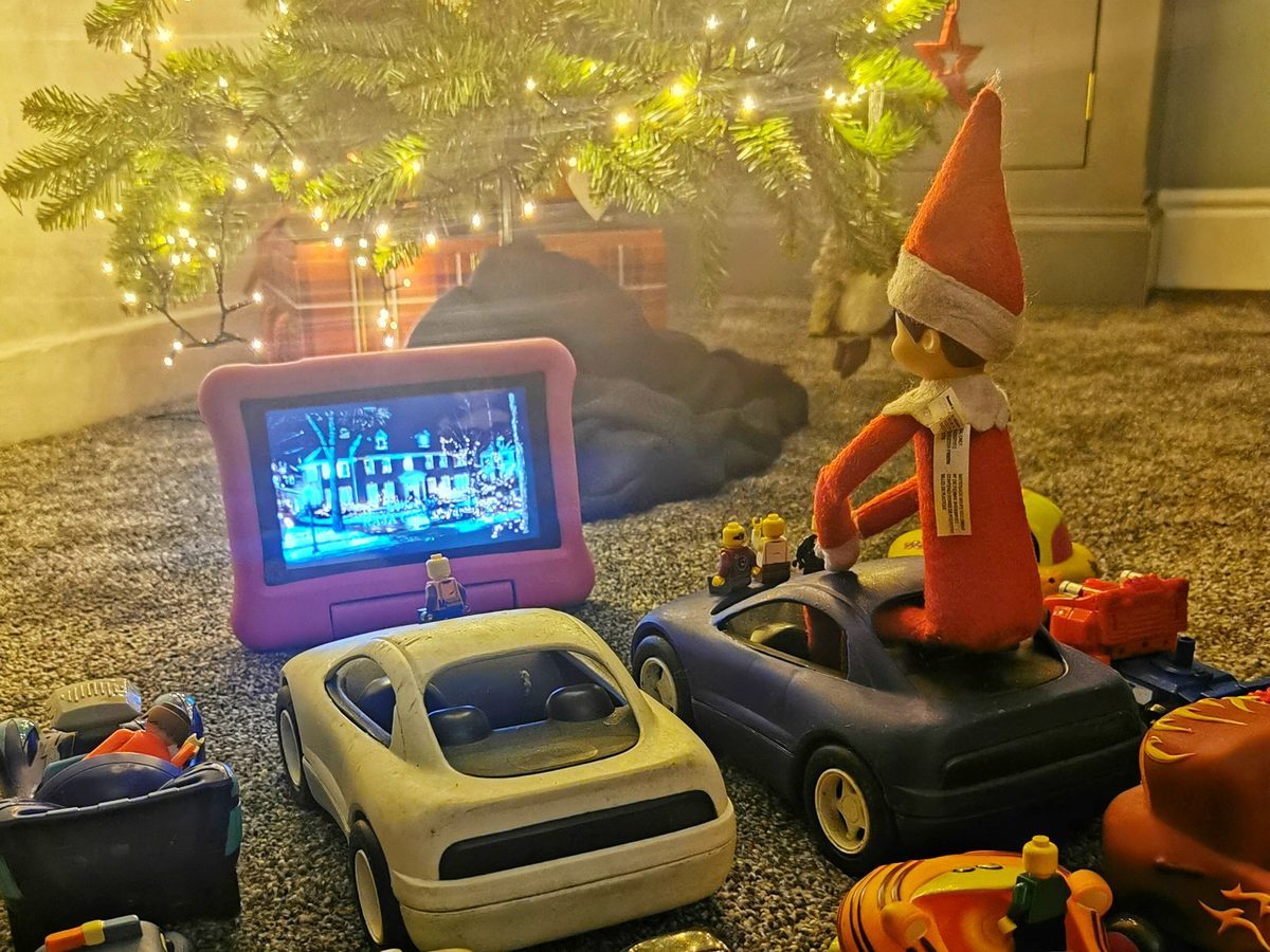Elf positioned as drive-in movie attendant with toy cars arranged in rows before screen.