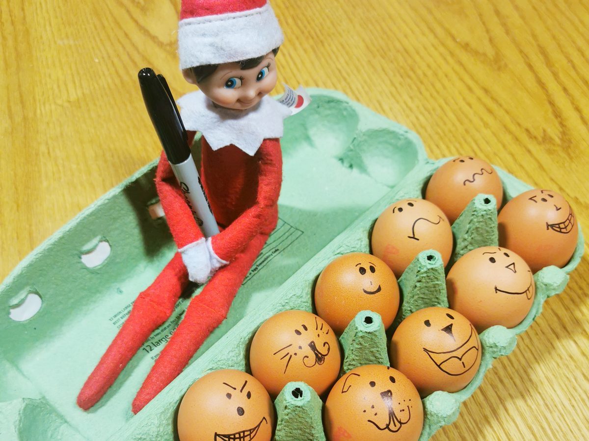 Elf surrounded by eggs decorated with silly drawn-on faces using markers.