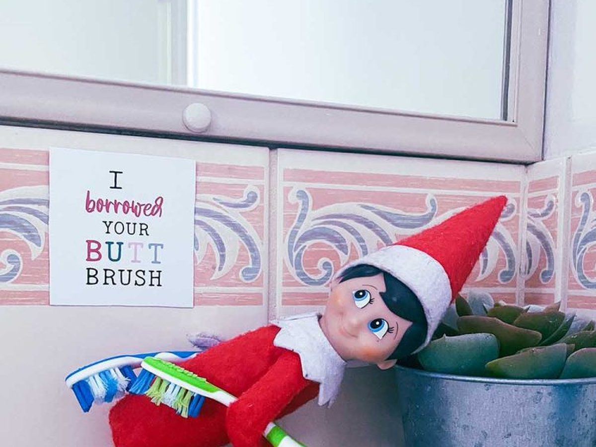 Elf positioned near toothbrushes in scrubbing pose with borrowed butt brush sign.