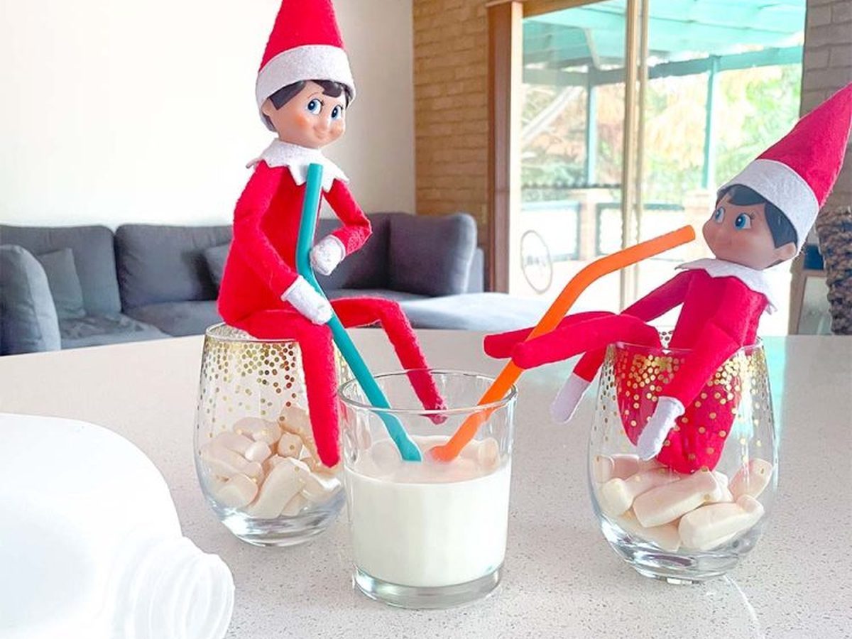 Two Christmas elves sitting in glasses of milk bottle candy drinking from milk containers.