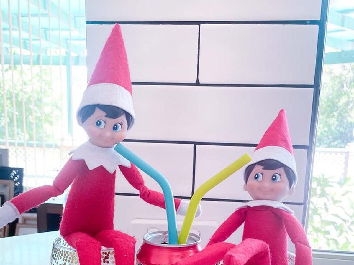 Two elf dolls sitting in glasses of Coke bottle gummies drinking from Coke cans.