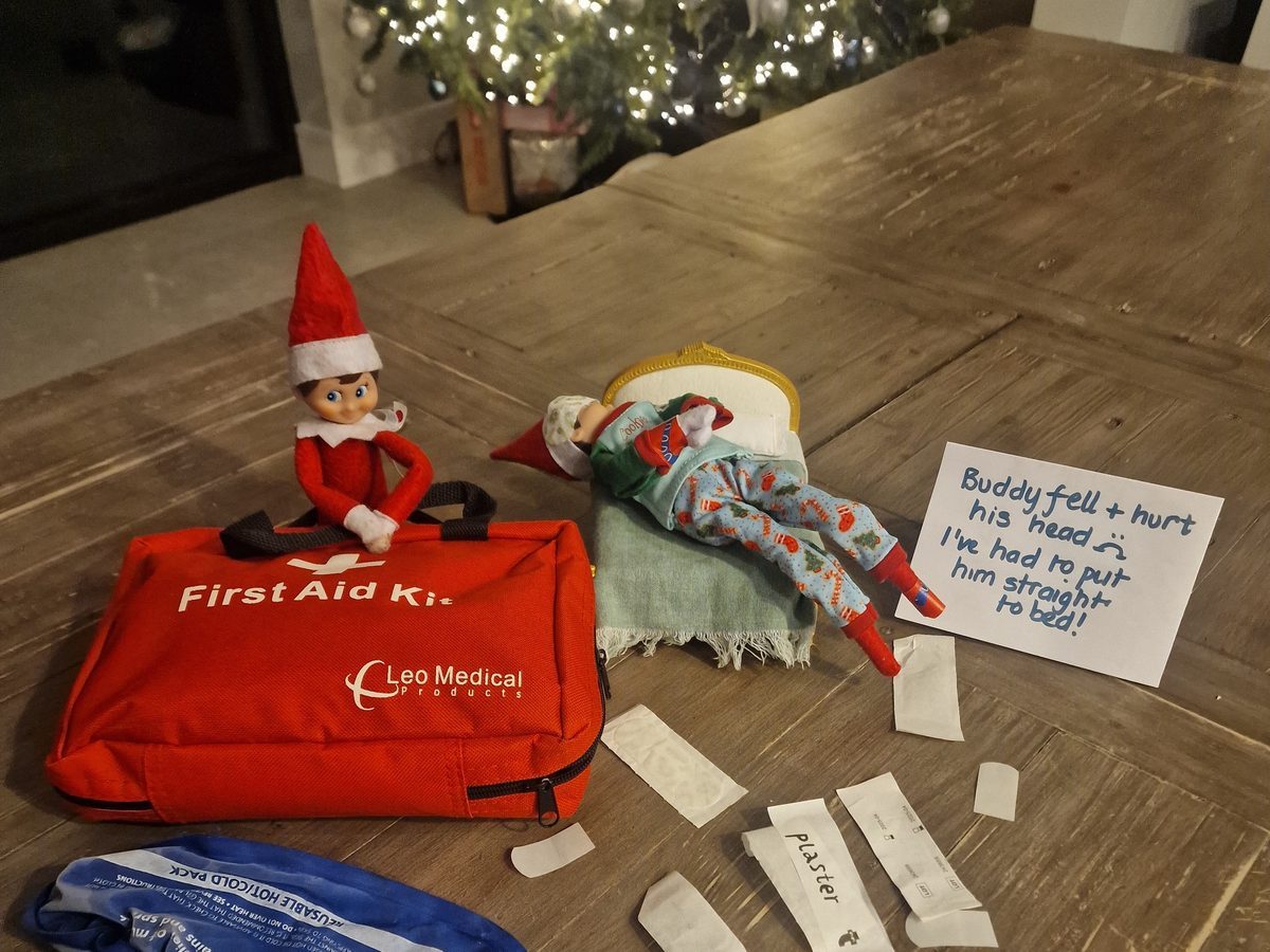 Elf bandaging stuffed toy with first aid supplies nearby.