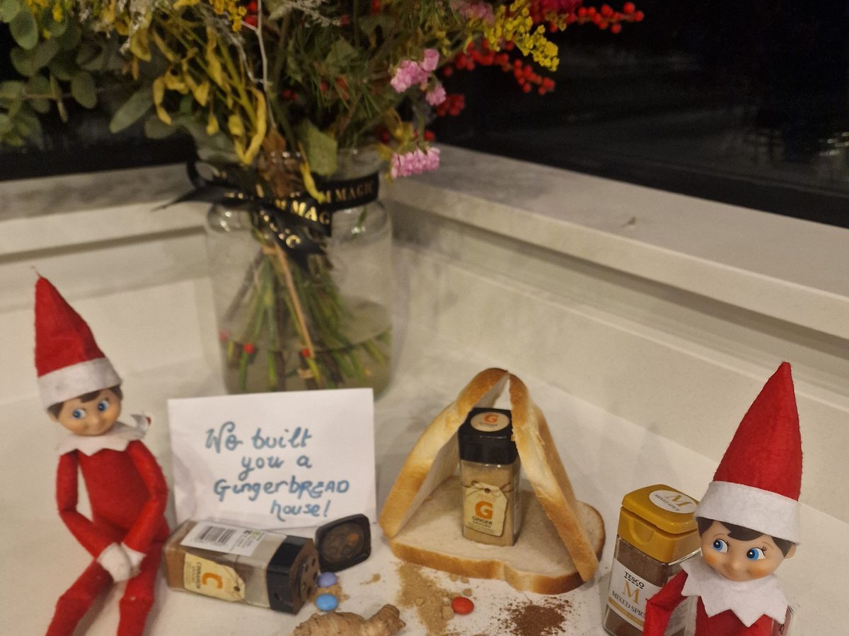 Elf building gingerbread house with icing and candy decorations visible.