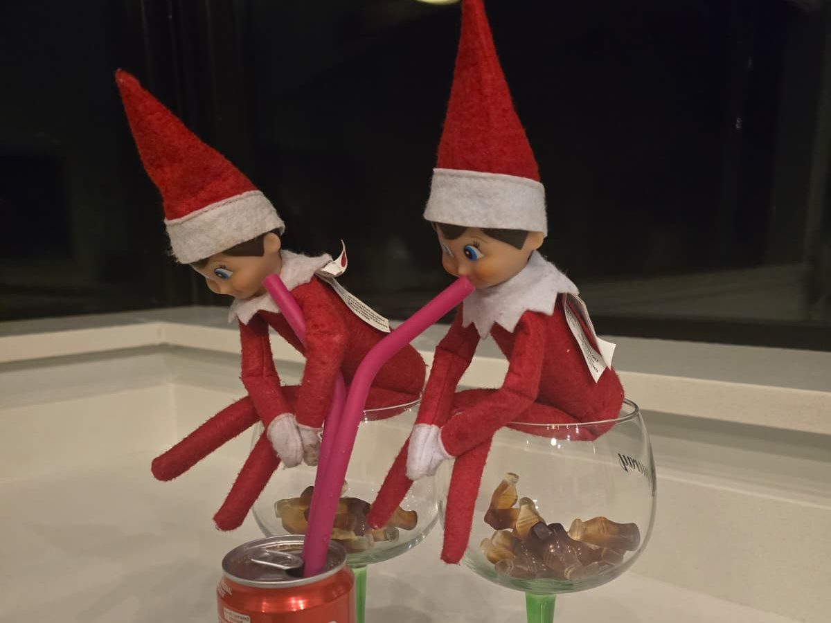 Elf beside giant gummy cola bottle with small straw as breakfast surprise.