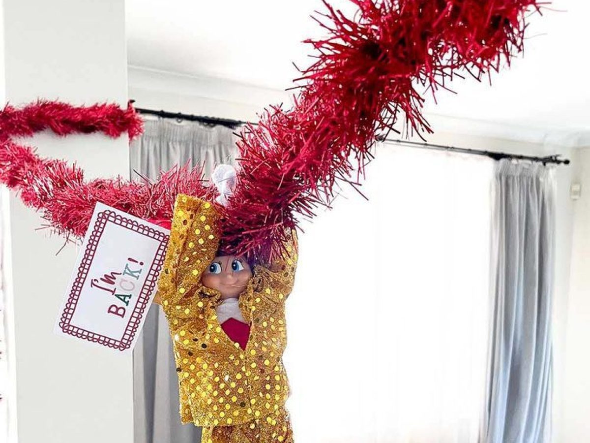 Elf in sparkly costume swinging from tinsel vine between two columns with I'm Back sign.