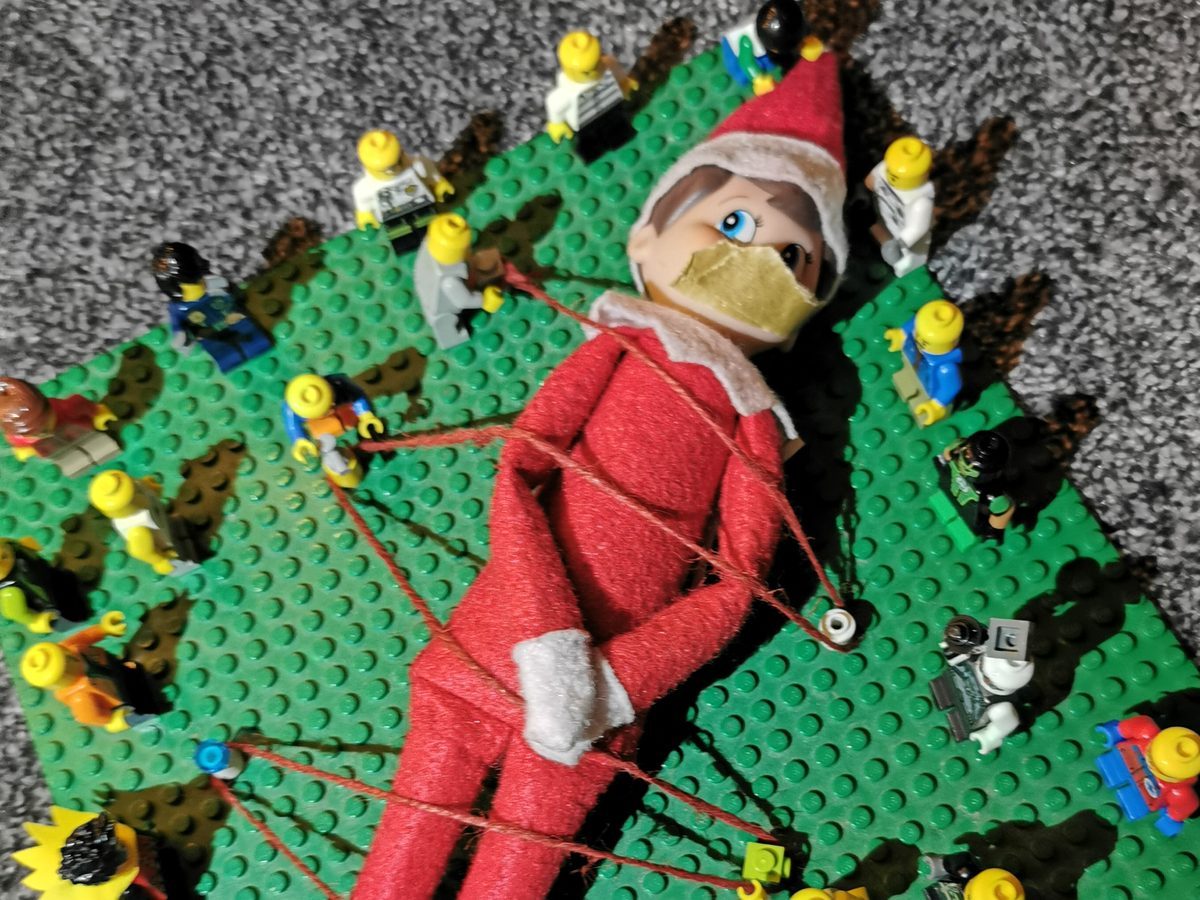 Elf bound with string surrounded by Lego minifigures wielding tiny weapons in attack formation.