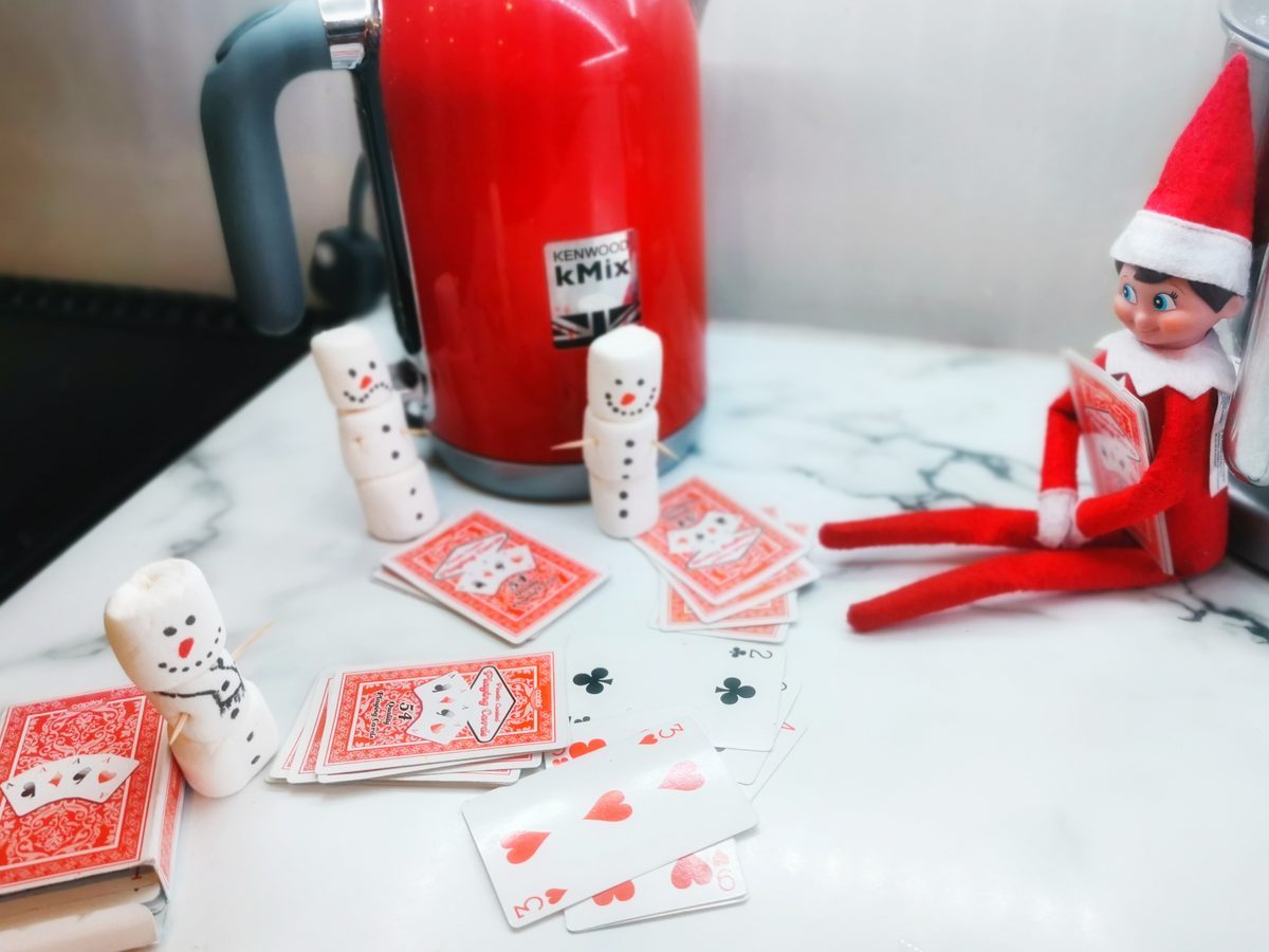 Marshmallow snowmen seated around table playing cards with elf dealer.