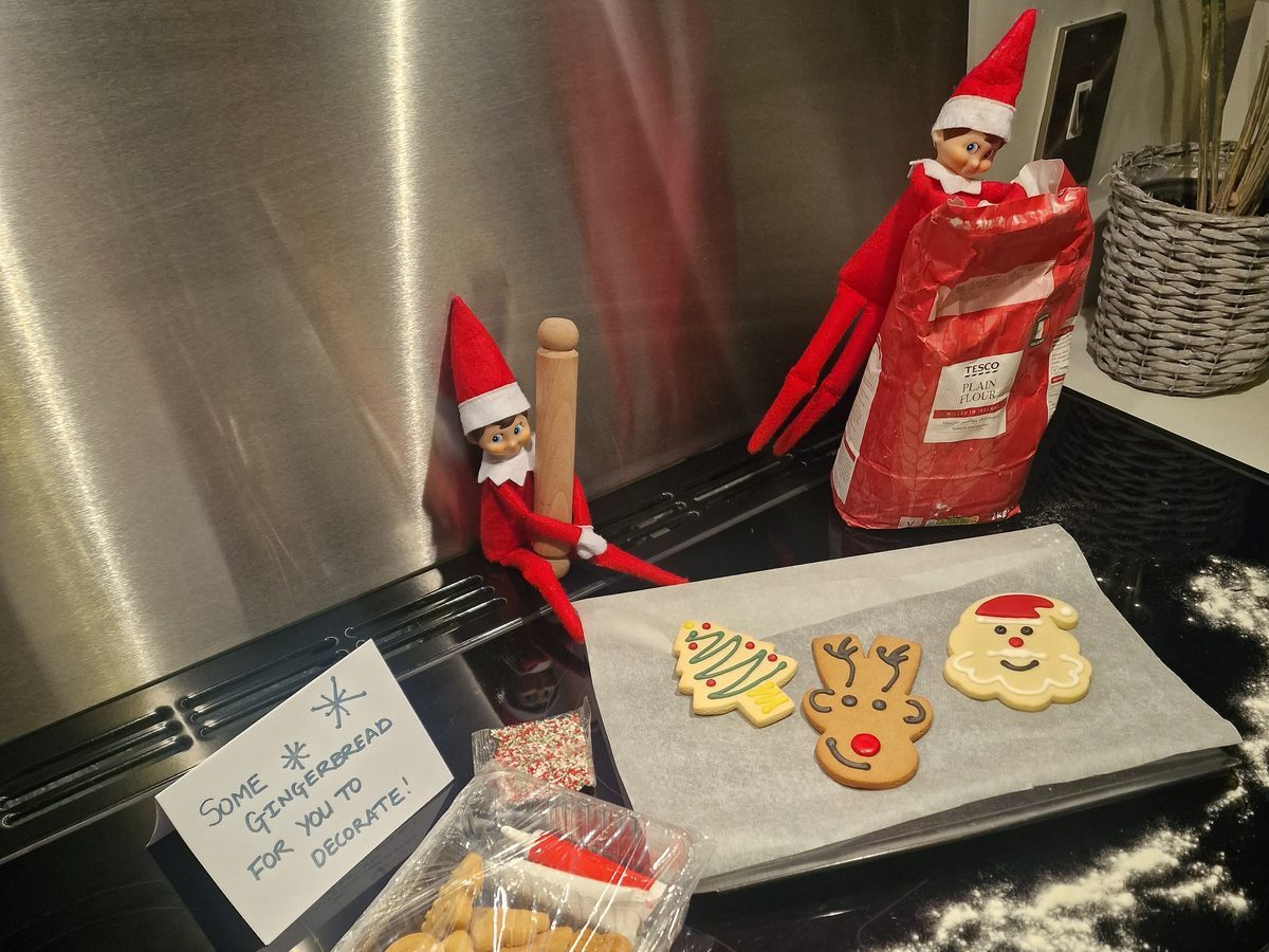 Elf surrounded by cookie dough, flour, and baking supplies on kitchen counter.