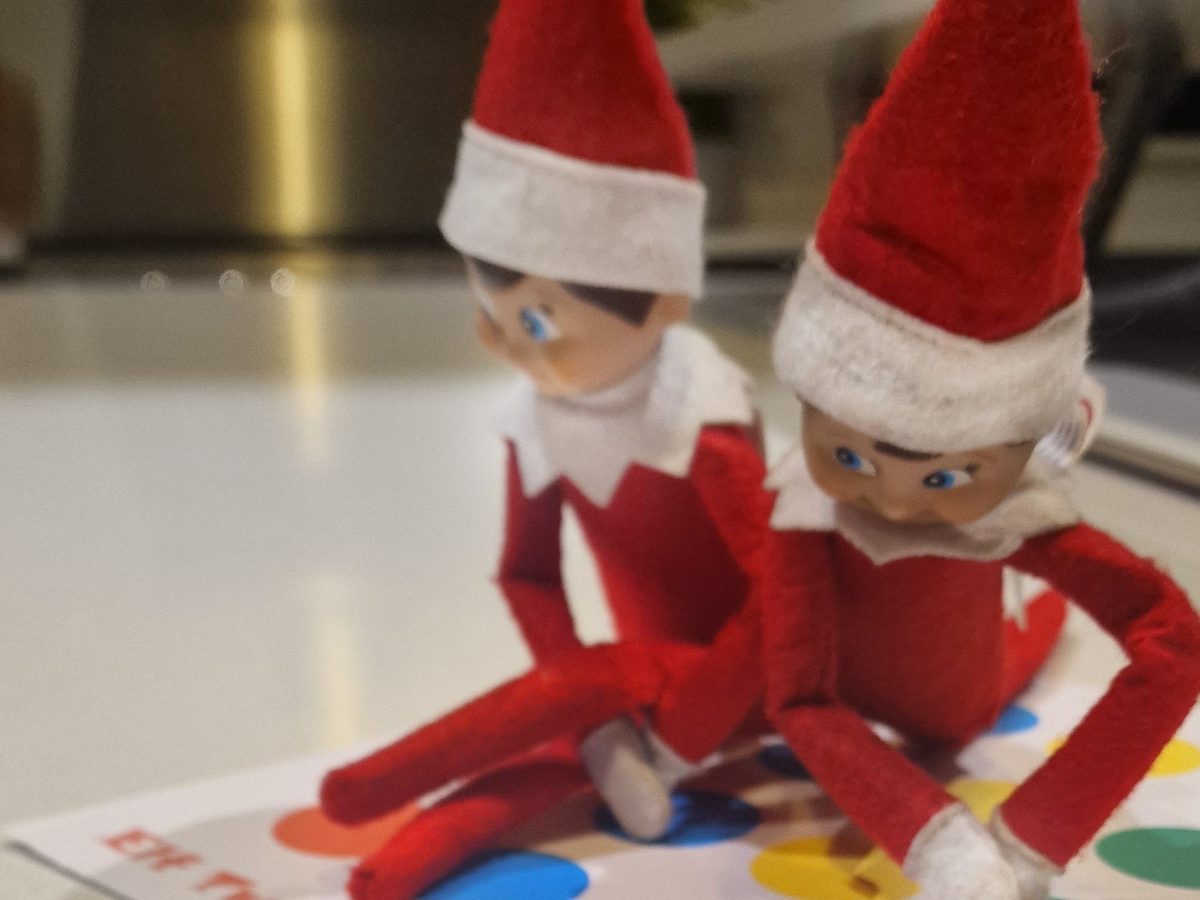 Elf in twisted pose on handdrawn Twister board with colored circles.