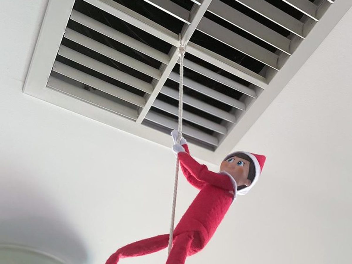 Elf suspended by string from ceiling vent in spy-style rappelling position.