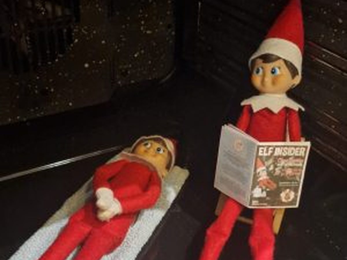 Elf lounging in oven with sunglasses and magazine, pretending to sunbathe.