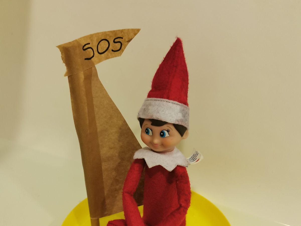 Elf sailing in paper boat floating in water-filled sink.