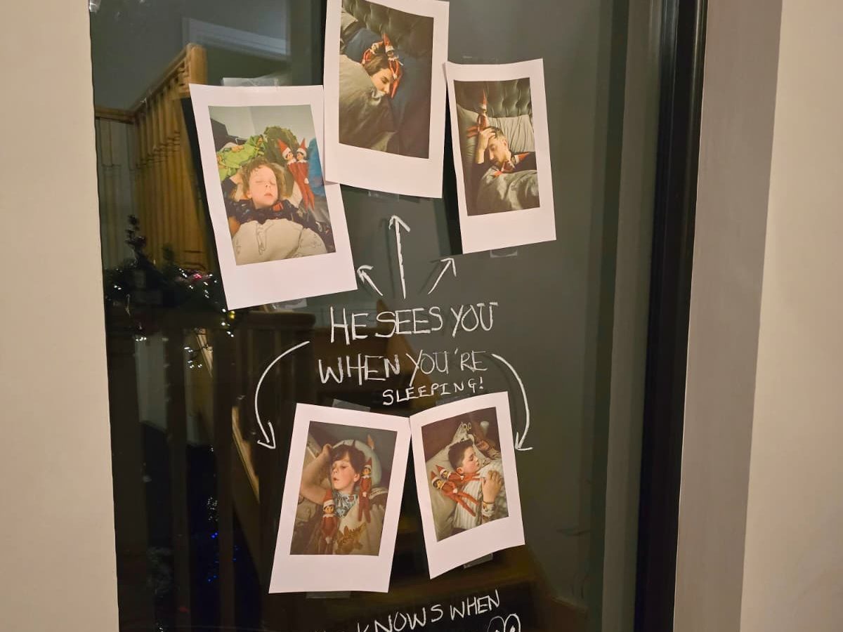 Elf positioned on pillow with camera taking selfie photos of sleeping family members.