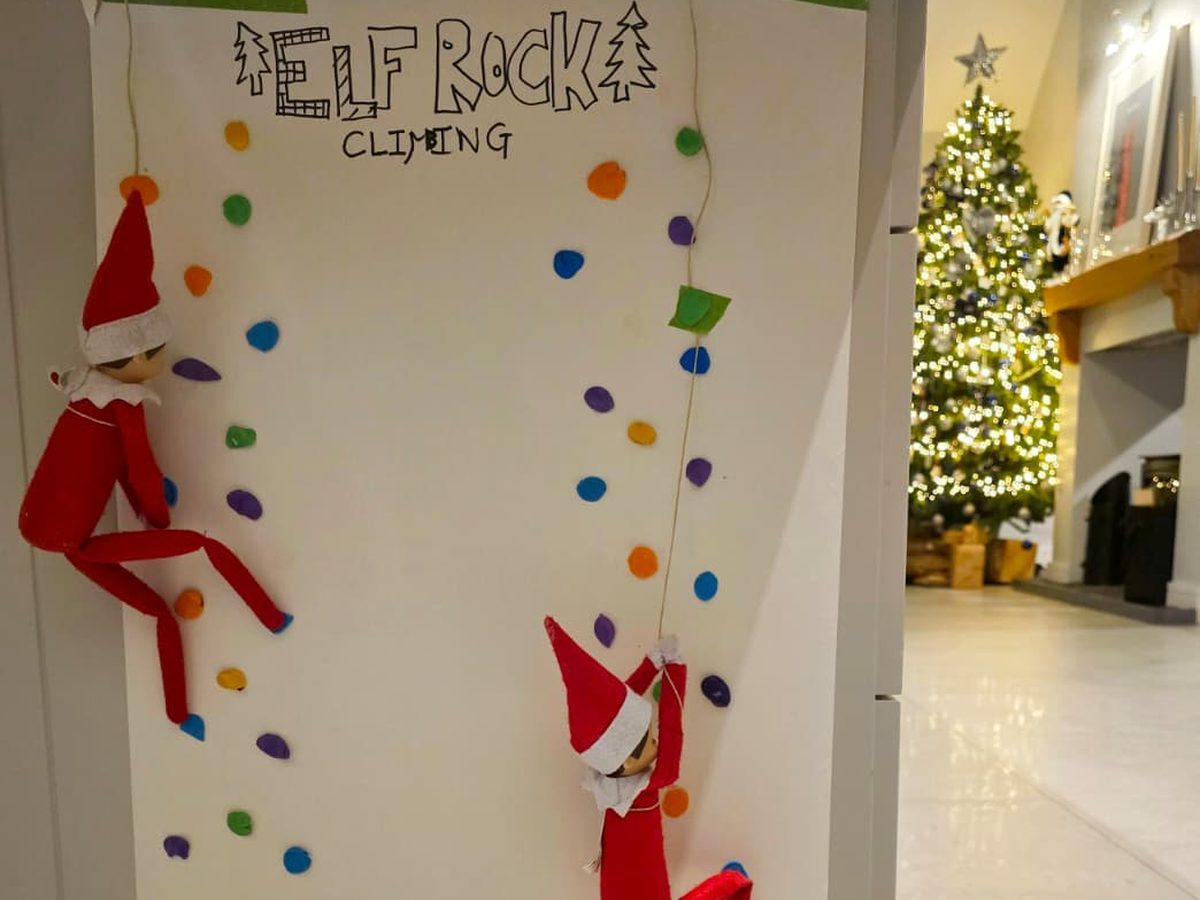 Elf mid-climb on Play-Doh holds attached to surface in challenging climbing race scenario.