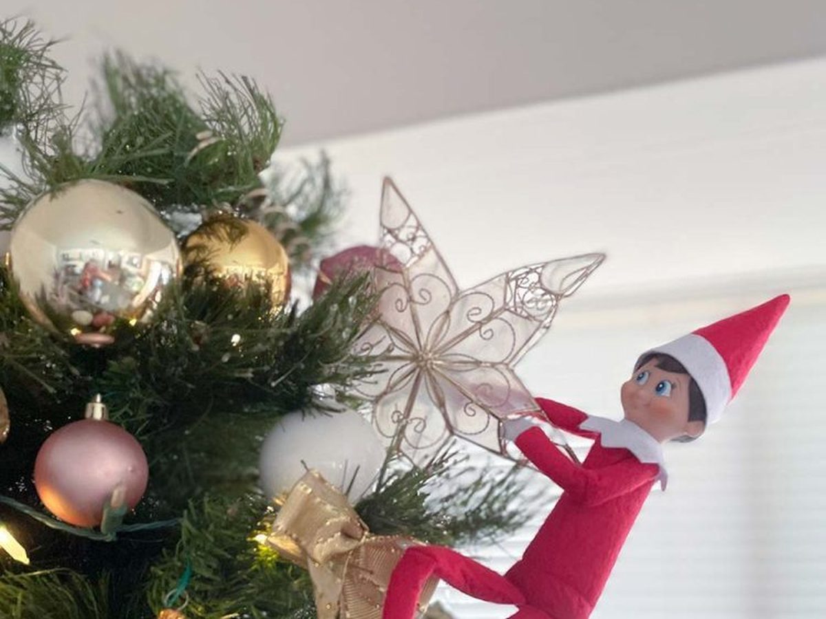 Elf positioned at Christmas tree top reaching down and pulling off star ornament.