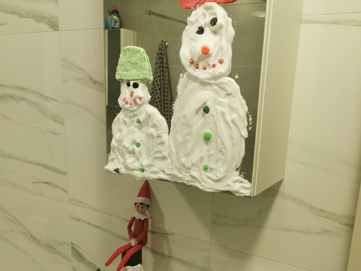 Elf beside shaving foam snowmen with carrot noses on plate or tray.