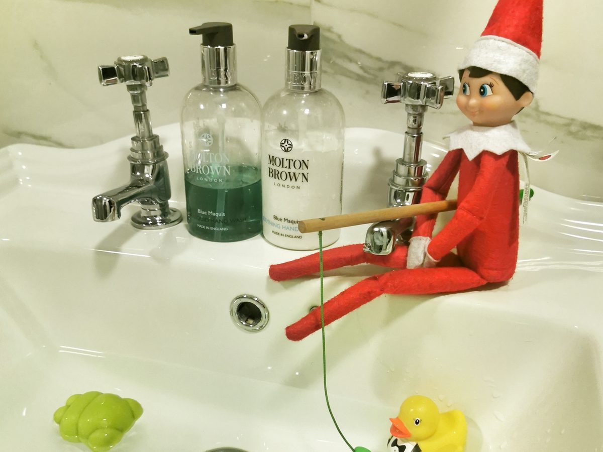 Elf holding toy fishing rod positioned over water-filled sink with small fish.