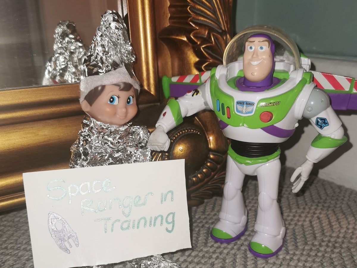 Elf positioned among toy astronaut figures and miniature spaceship in training scenario.