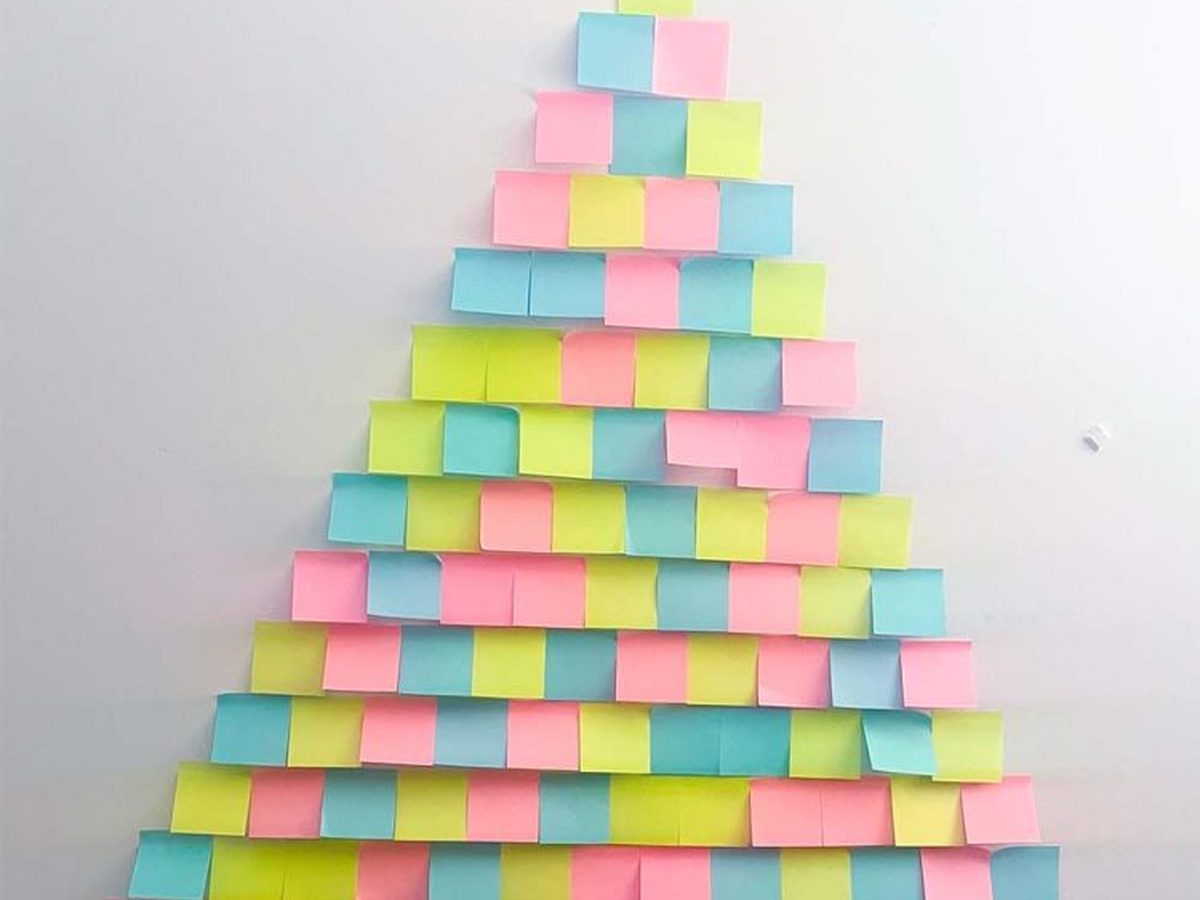 Two elves on floor beside large sticky note Christmas tree on wall with yellow star.