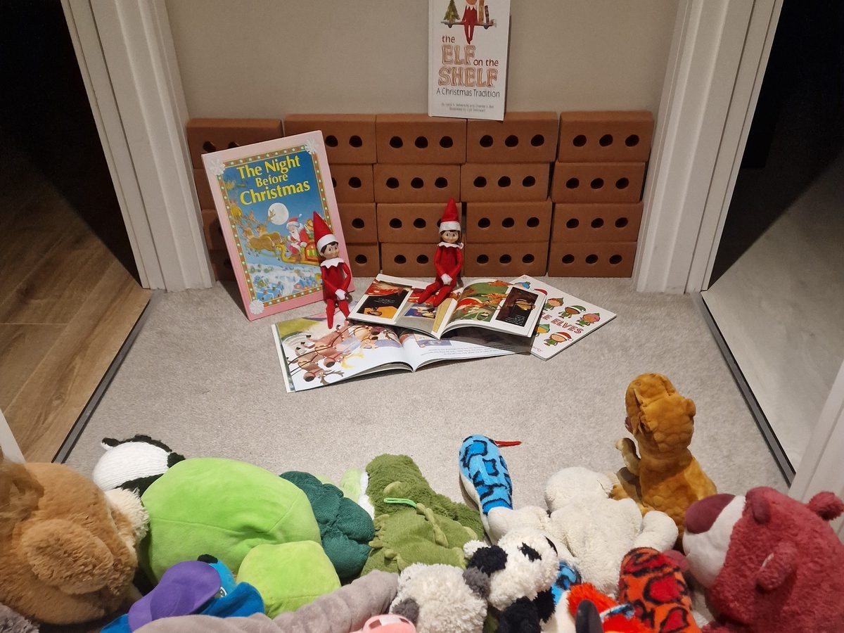 Elf reading Christmas book to gathered toys and stuffed animals.