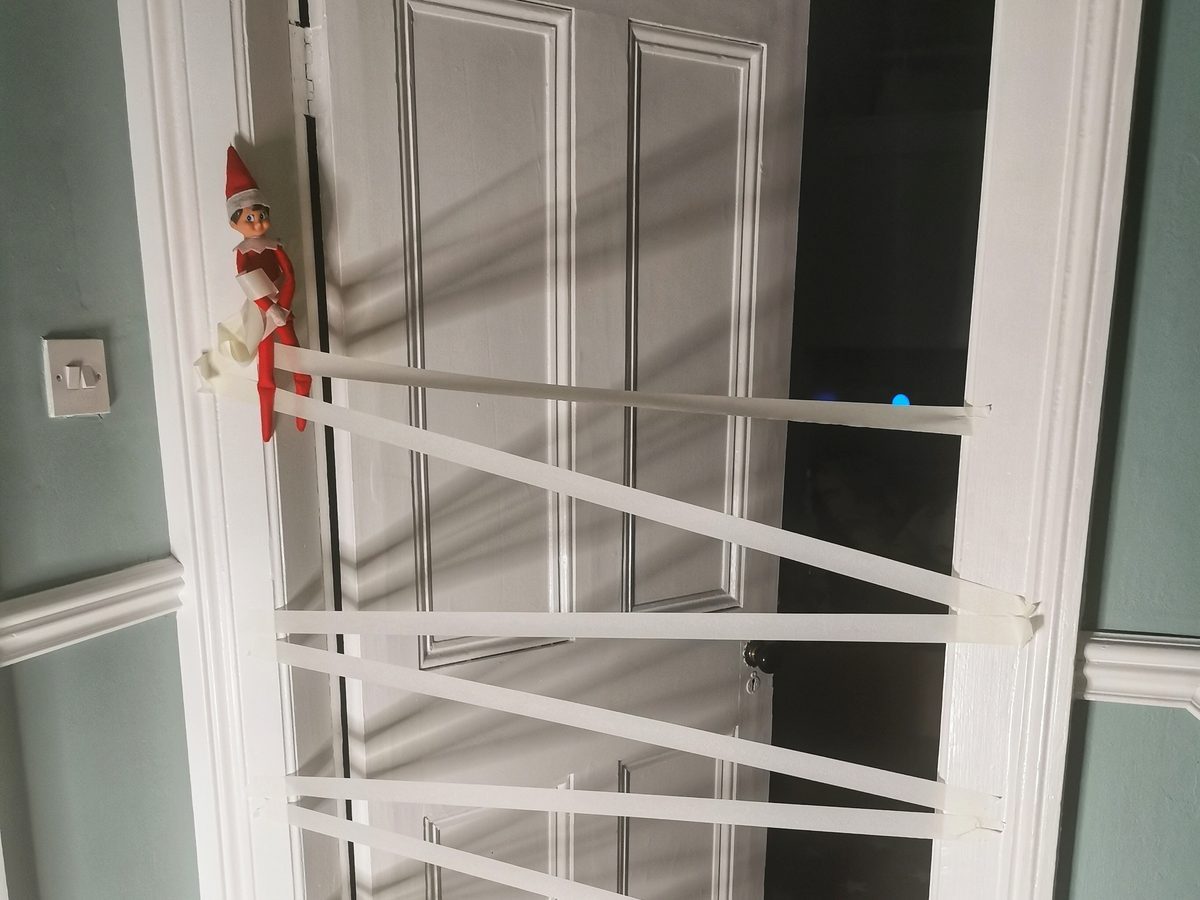 Elf positioned at door covered with criss-crossed painter's tape forming impassable barrier.