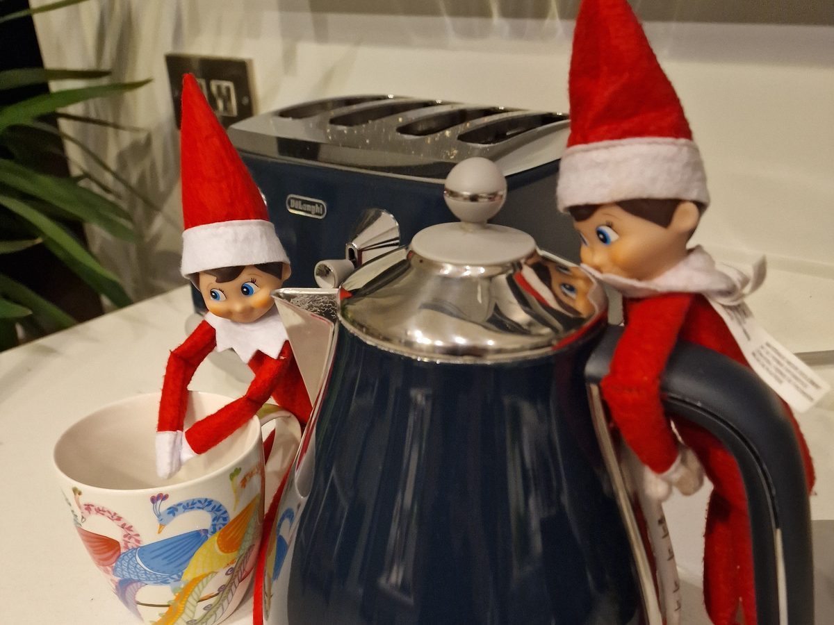 Elf positioned at tiny tea service with cup and saucer on kitchen counter.
