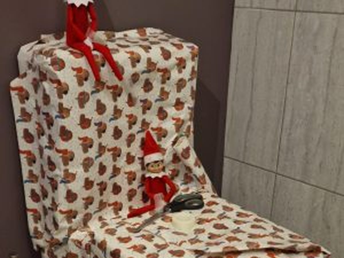 Toilet wrapped with festive ribbon and paper with elf positioned on top.