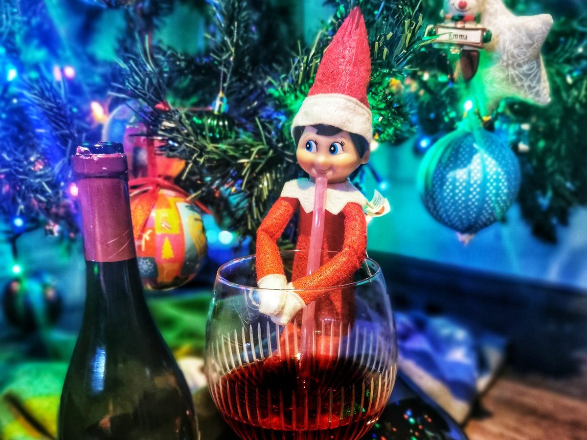Elf enjoying festive drink in thimble with holiday-themed wine tasting setup.